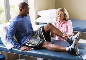 Physical therapist examining African American man (20s) on treatment table.
