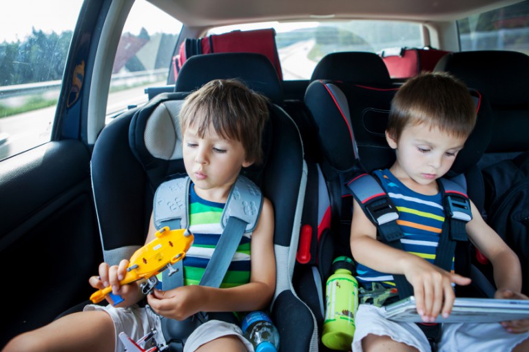 Two boy in children car seats, traveling by car and playing with toys and tablet, summertime